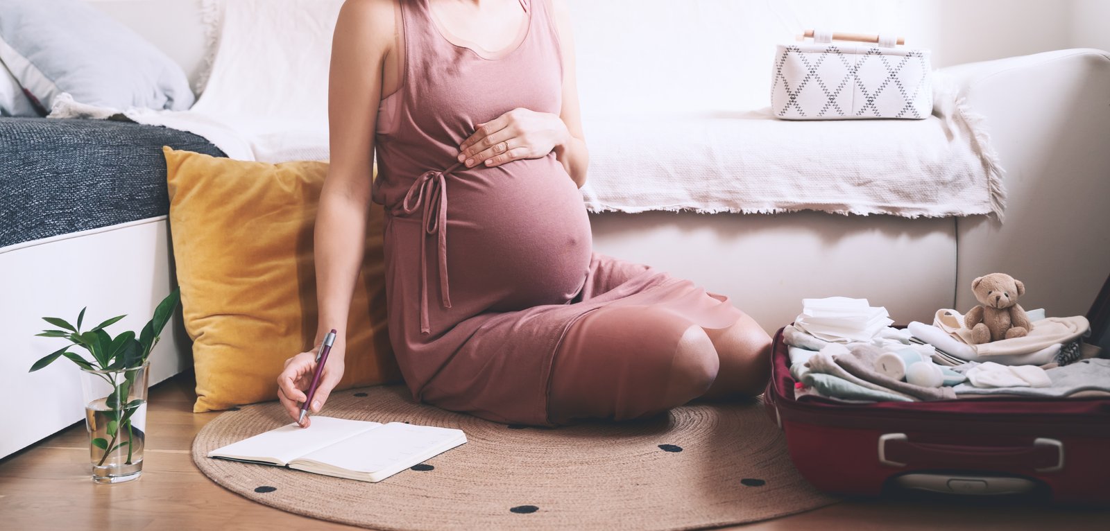 Expectant mother with suitcase of baby stuff preparing for newborn birth during pregnancy.