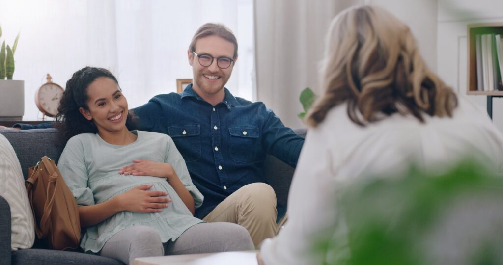 Ein Paar bei der geburtspsychologischen Beratung, sitzt auf einer Couch und redet miteinander.