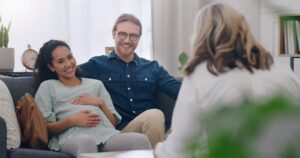 Ein Paar bei der geburtspsychologischen Beratung, sitzt auf einer Couch und redet miteinander.
