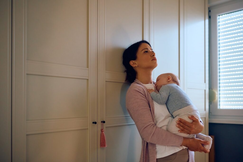 Young sad mother holding her sleeping baby in her arms at home after a traumatic birth.